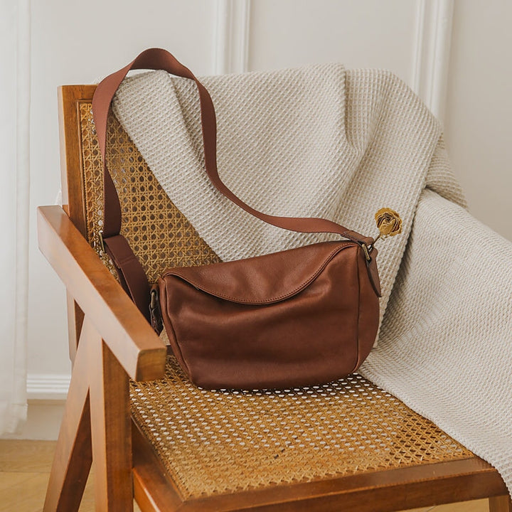Brown leather crescent crossbody bag resting on a rattan chair, vintage saddle style