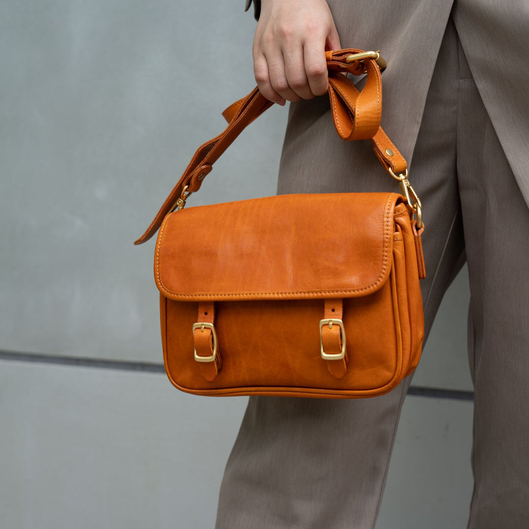 Woman holding a tan vegetable tanned leather crossbody bag with double gold buckles