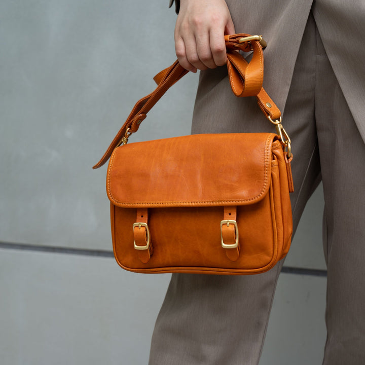Woman holding a tan vegetable tanned leather crossbody bag with double gold buckles