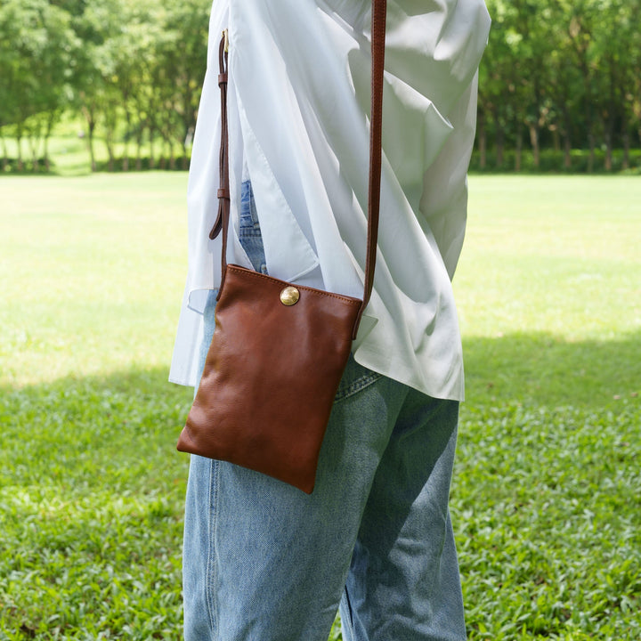 Woman wearing a vegetable tanned leather crossbody phone bag in brown over a casual outfit