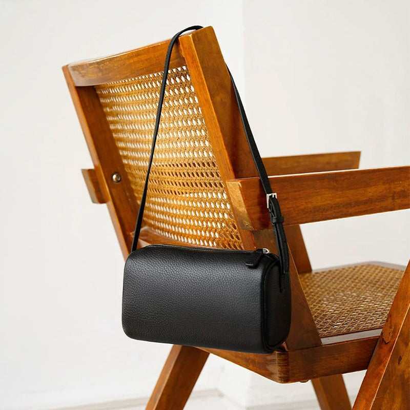 Leather cylinder bag in black with adjustable crossbody strap on a rattan chair