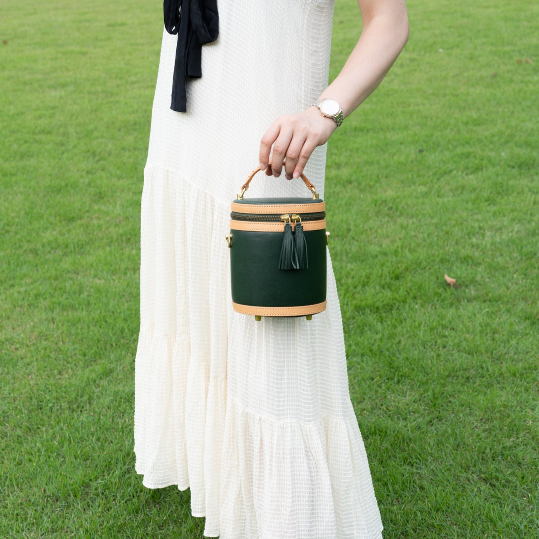 Woman holding a dark green leather cylinder bag with tassel zip on a lawn