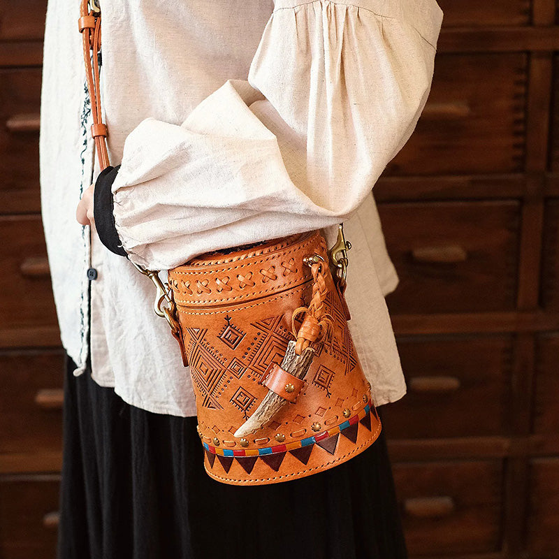 Model wearing a leather cylinder crossbody bag with geometric tooling and an antler latch.