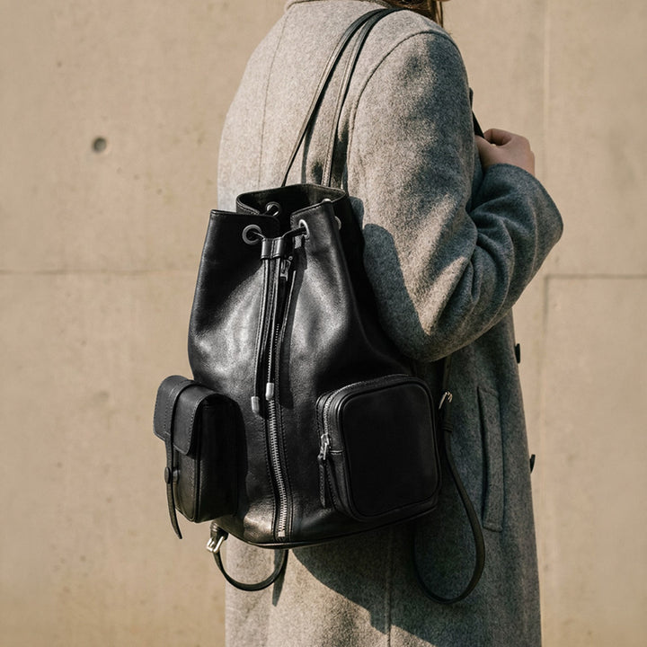 Vegetable tanned leather drawstring bucket backpack in black with front zip pockets and adjustable straps.