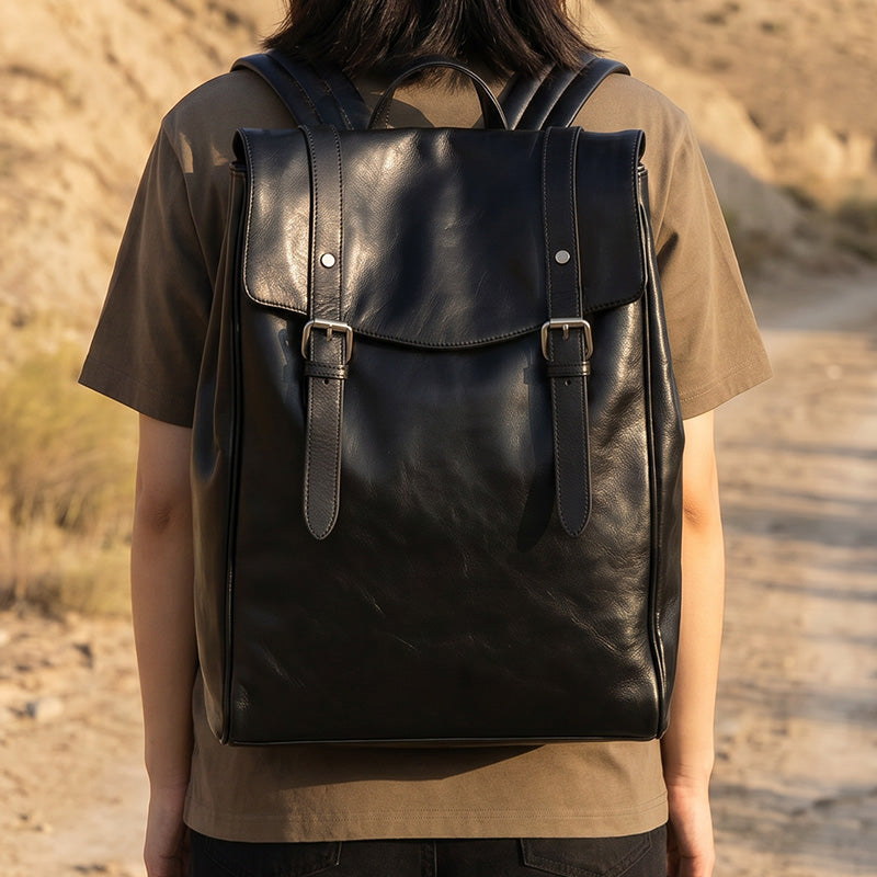 Black vegetable-tanned leather flap backpack with top handle and adjustable straps — front view