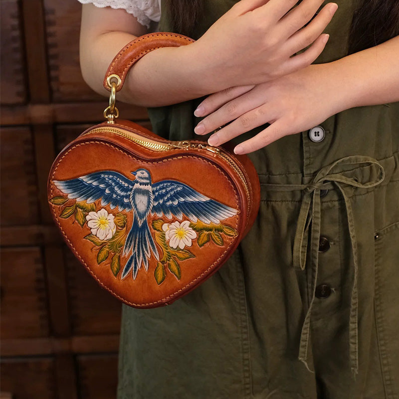 Woman carrying a hand-tooled leather heart shaped crossbody bag by its top handle