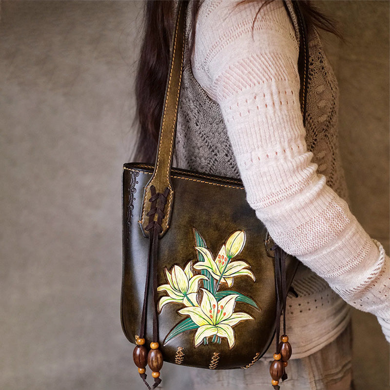 A woman carries a leather bucket tote bag with white lily artwork and wooden bead accents.