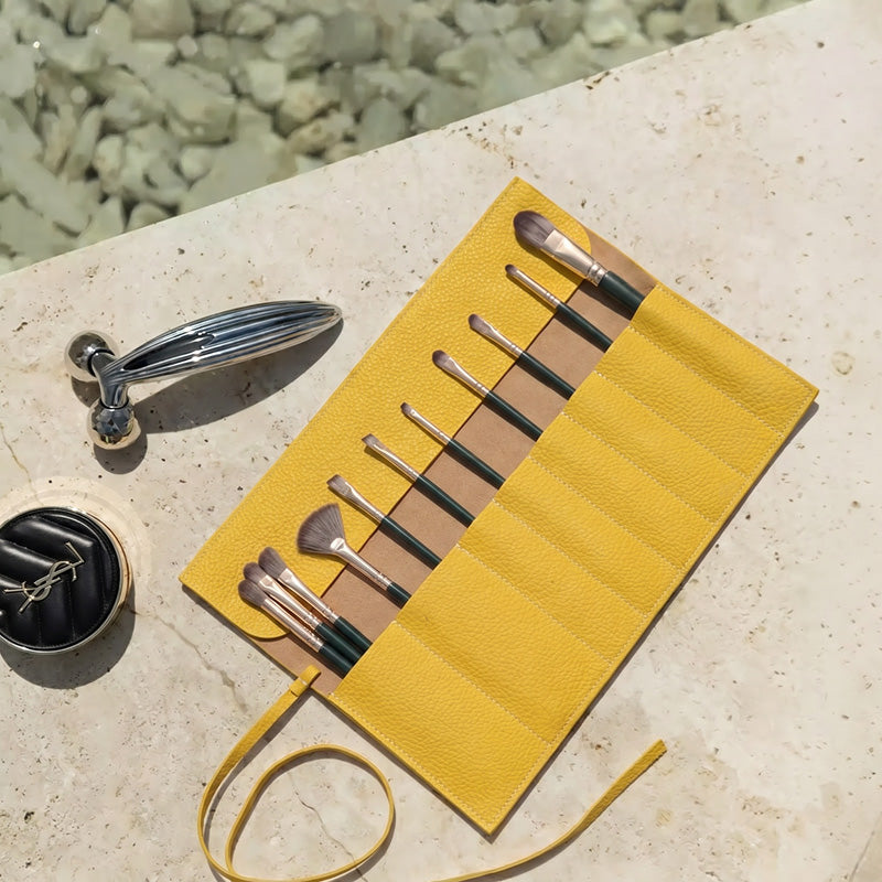 Yellow leather makeup brush roll unrolled with brushes organized in slots