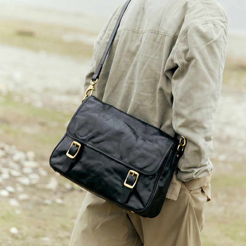 Vintage vegetable tanned leather messenger bag in black with double gold buckle flap closure and adjustable strap.