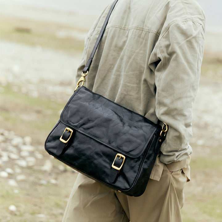 Vintage vegetable tanned leather messenger bag in black with double gold buckle flap closure and adjustable strap.
