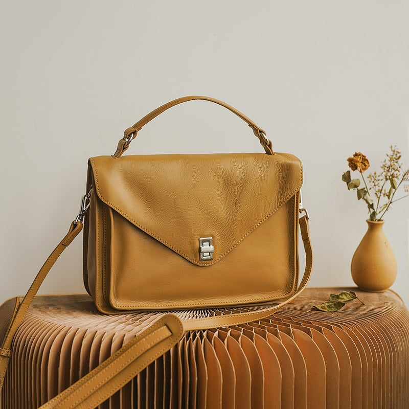 Yellow leather satchel bag with twist lock sitting on a decorative surface