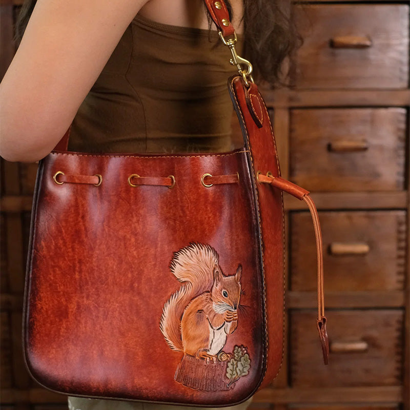 A woman carries a brown leather shoulder bag with a hand-carved squirrel motif.