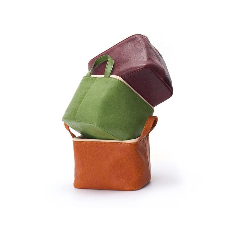 Three handmade leather storage baskets stacked in yellow, green, and burgundy