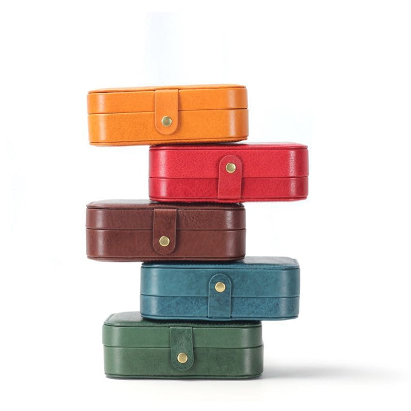 Small leather travel jewelry boxes stacked in five colors — yellow, red, brown, blue and green
