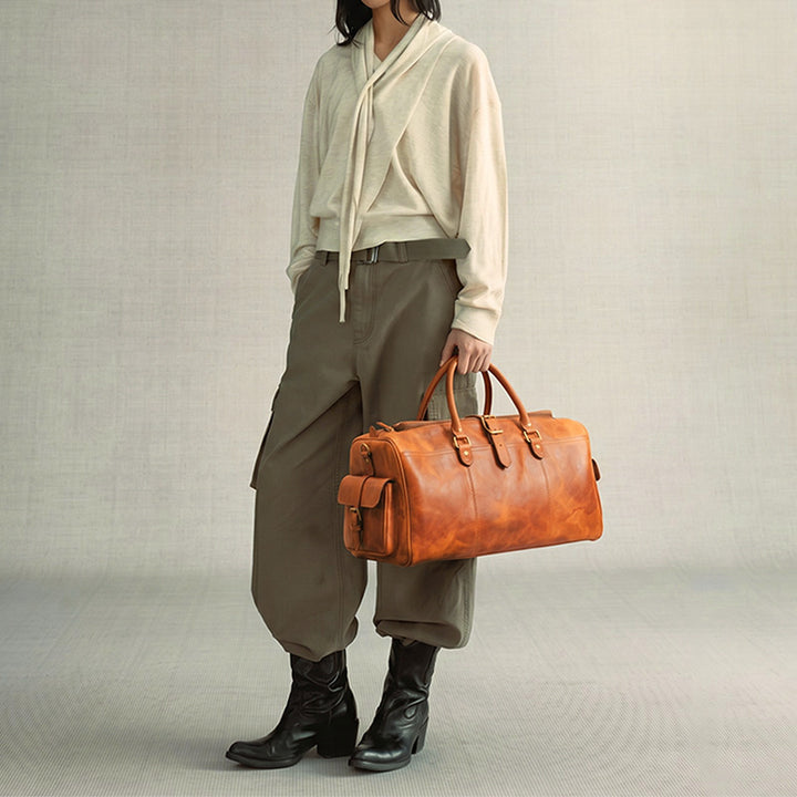 Sunset yellow vegetable-tanned leather weekender bag with signature side buckle pockets and gold hardware for travel.