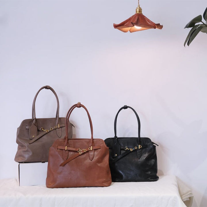 Brown, gray and black leather work tote bags with gold belt detail displayed on a shelf