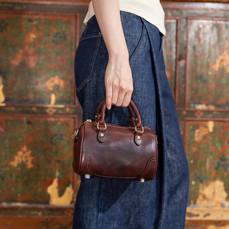 Woman holding a coffee vegetable tanned leather mini Boston bag by twin top handles, side view