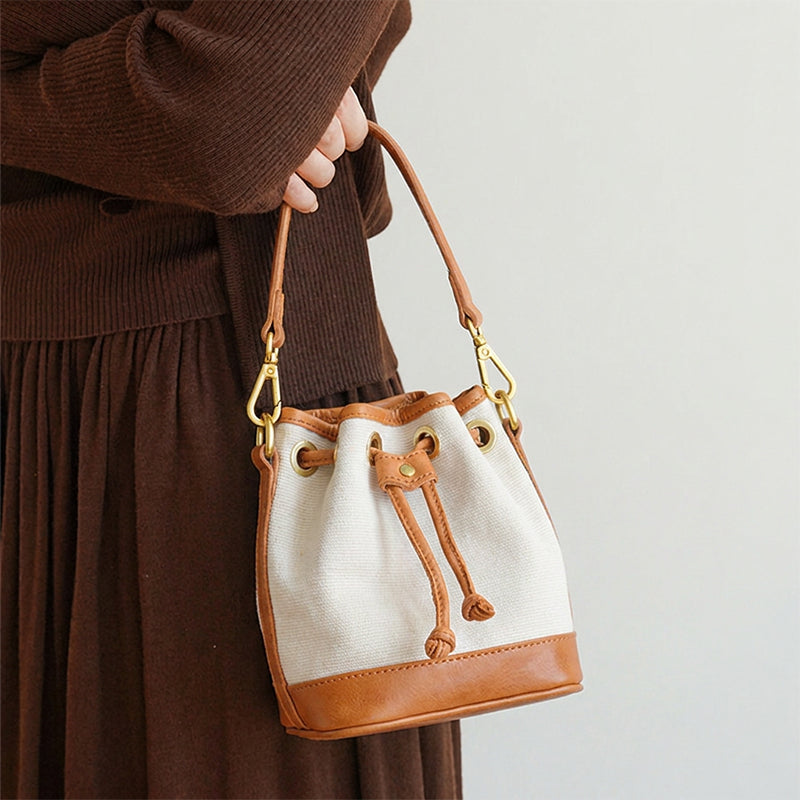 Woman holding a mini canvas bucket bag with leather trim and brass drawstring closure