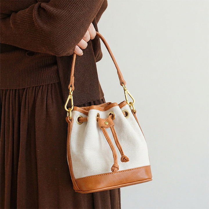 Woman holding a mini canvas bucket bag with leather trim and brass drawstring closure