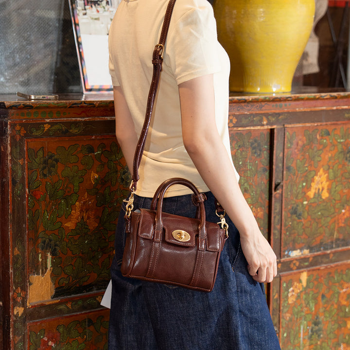 Woman wearing a brown full grain leather mini satchel bag with gold twist lock, side view