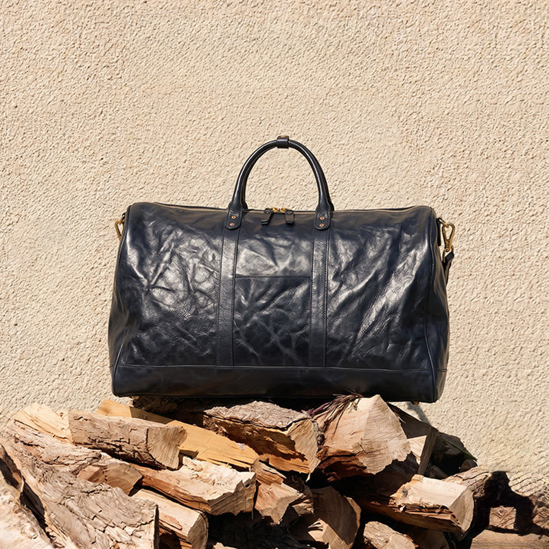 Oversized black leather duffle bag with cloud-grain vegetable-tanned leather and gold hardware, perfect for weekend travel.