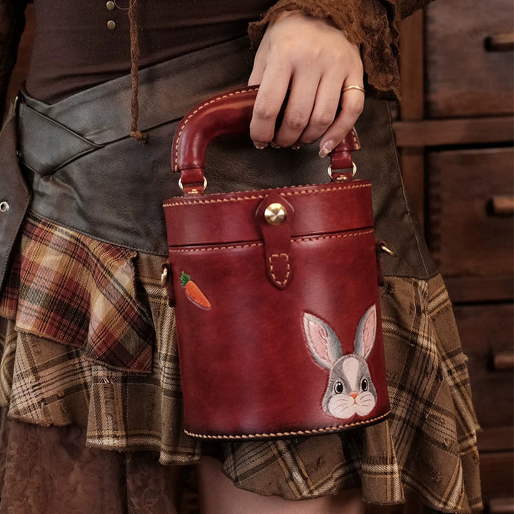 Woman holding a red leather cylinder bag with hand-tooled rabbit artwork.
