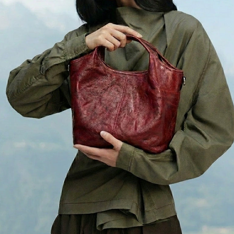 Model holding a red leather top handle bag with a crinkled texture.