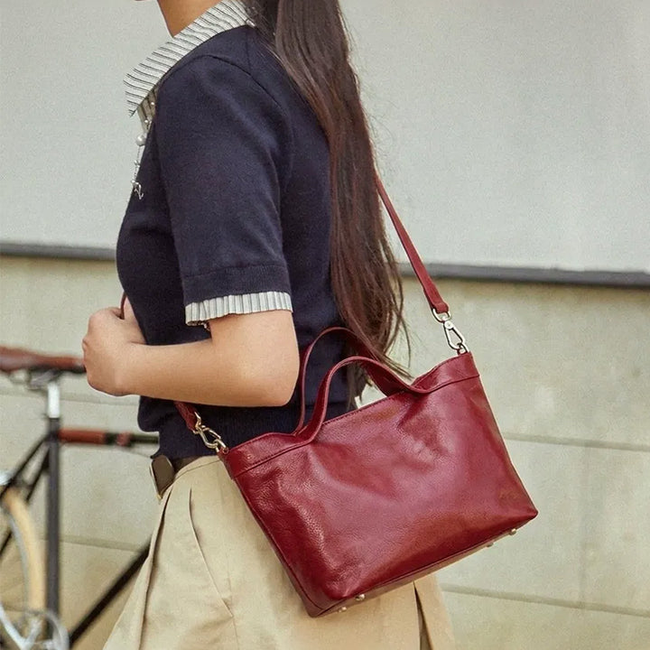 Woman carrying a red leather top handle tote bag on her shoulder.