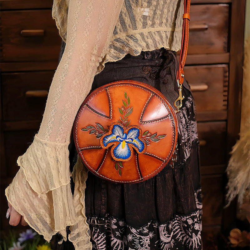 Brown round leather bag with hand-carved iris artwork, worn crossbody