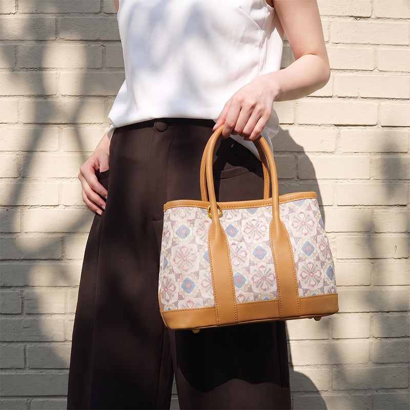 Woman holding a silk jacquard mini tote bag with floral brocade pattern and khaki leather trim