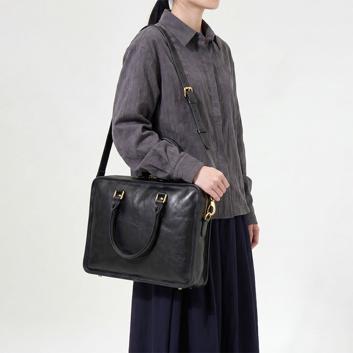 Slim black leather briefcase for women with arched handles and gold hardware, a structured vegetable-tanned laptop work bag.