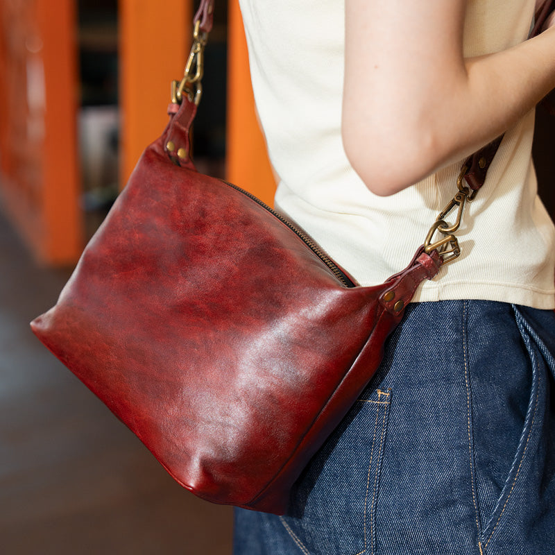 Woman wearing a brown top grain leather slouchy crossbody bag with brass zip top, side view