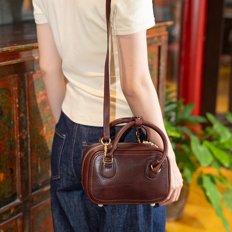 Woman carrying a coffee top grain leather small bowling bag with brass zip as shoulder, side view