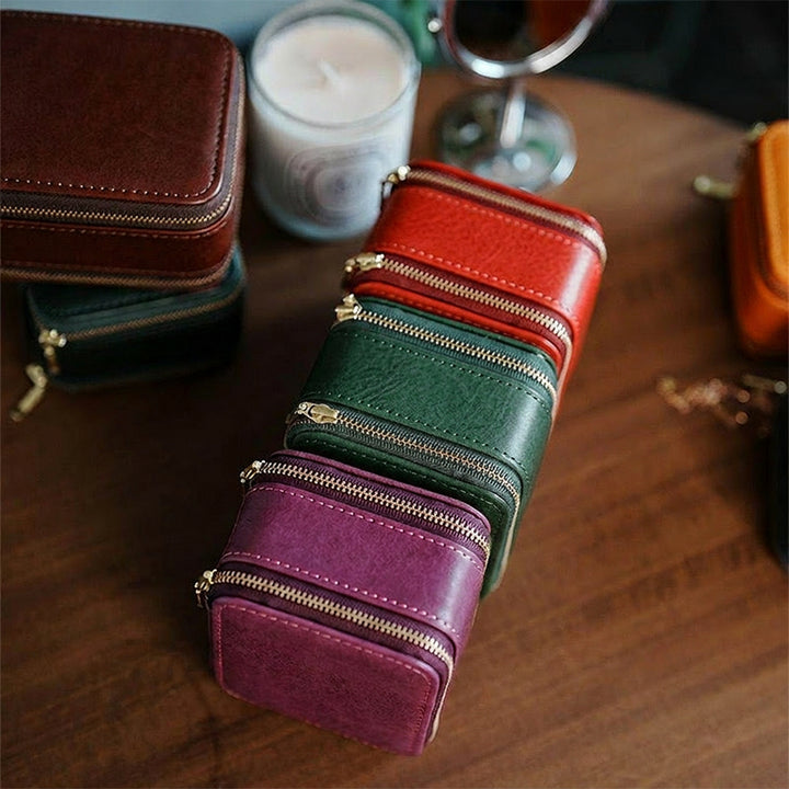 Small leather travel jewelry box with dual zipper, open showing two velvet-lined compartments for rings and bracelets.