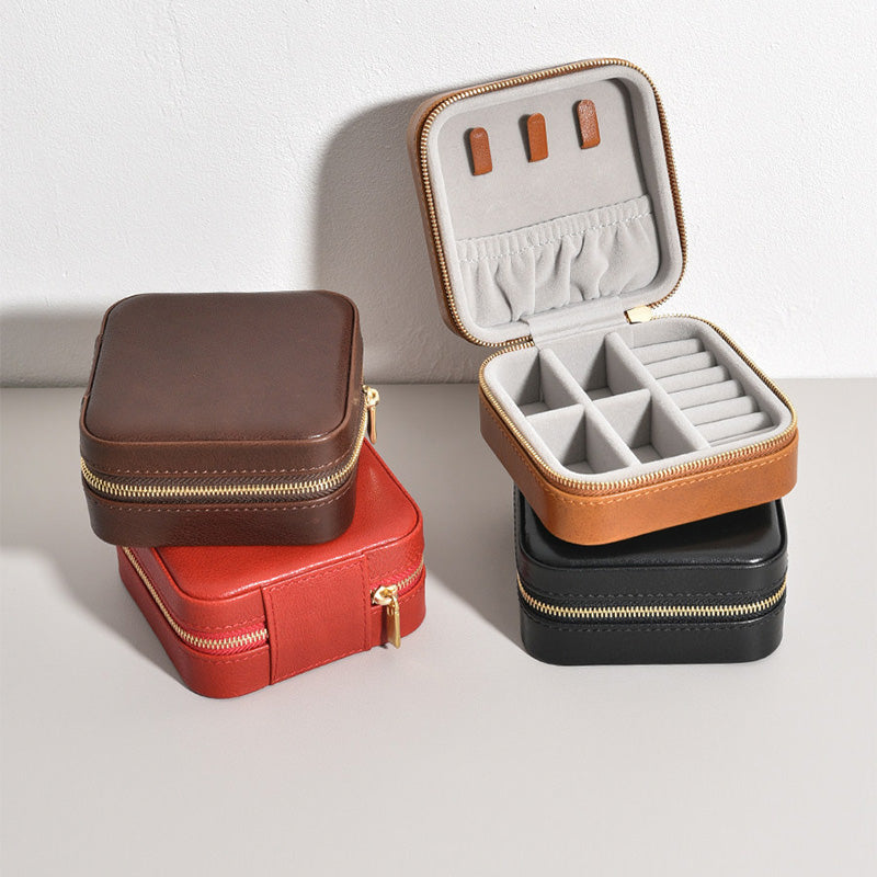 Small leather jewelry box with full zipper closure, open showing ring rolls, earring slots and velvet-lined compartments.