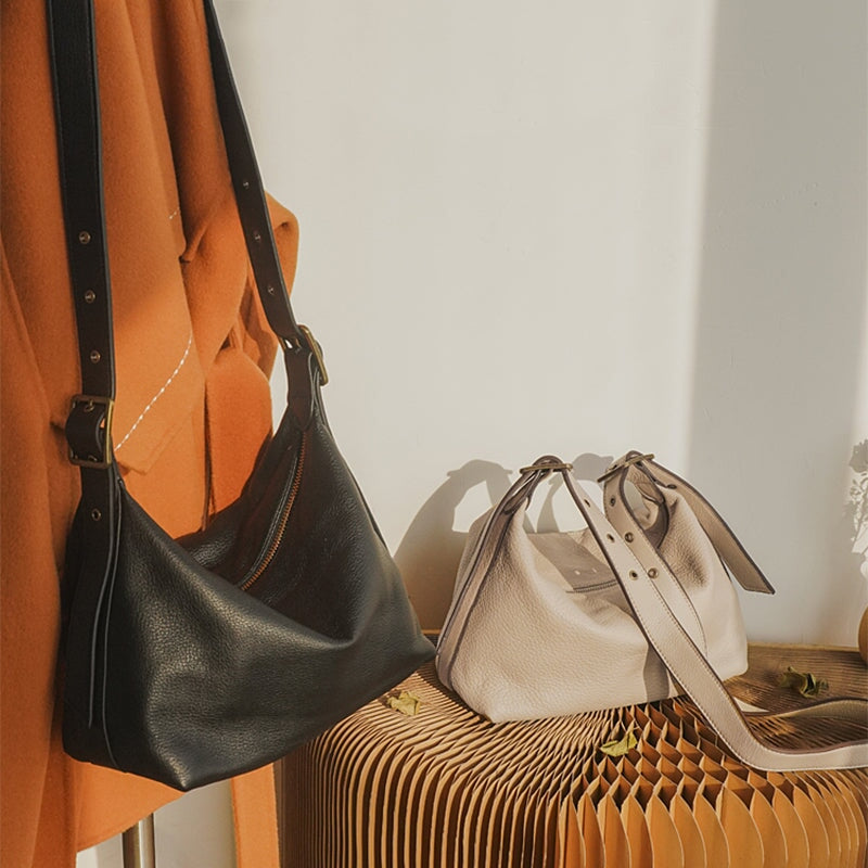 Black soft leather hobo bag hanging on a wall hook beside a white bag