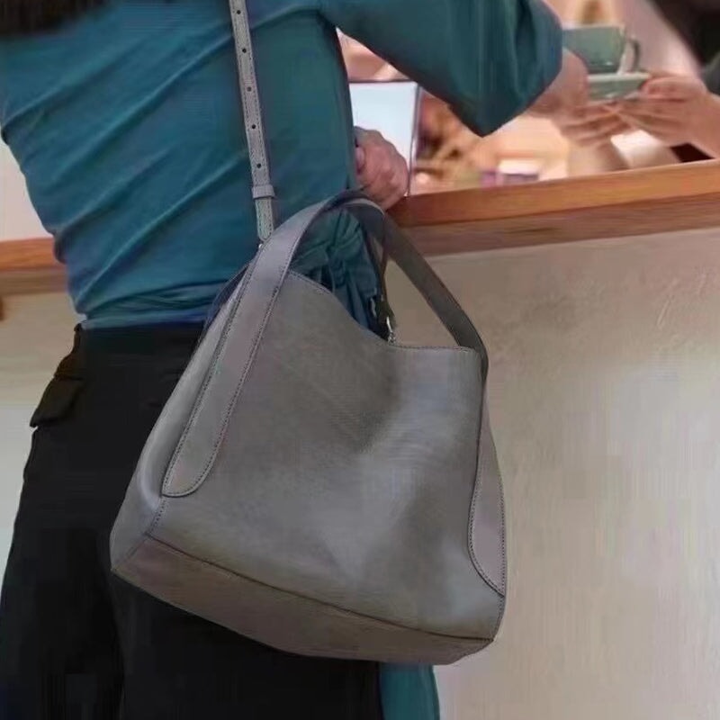 Woman carrying a soft leather hobo tote bag in gray over shoulder at a café