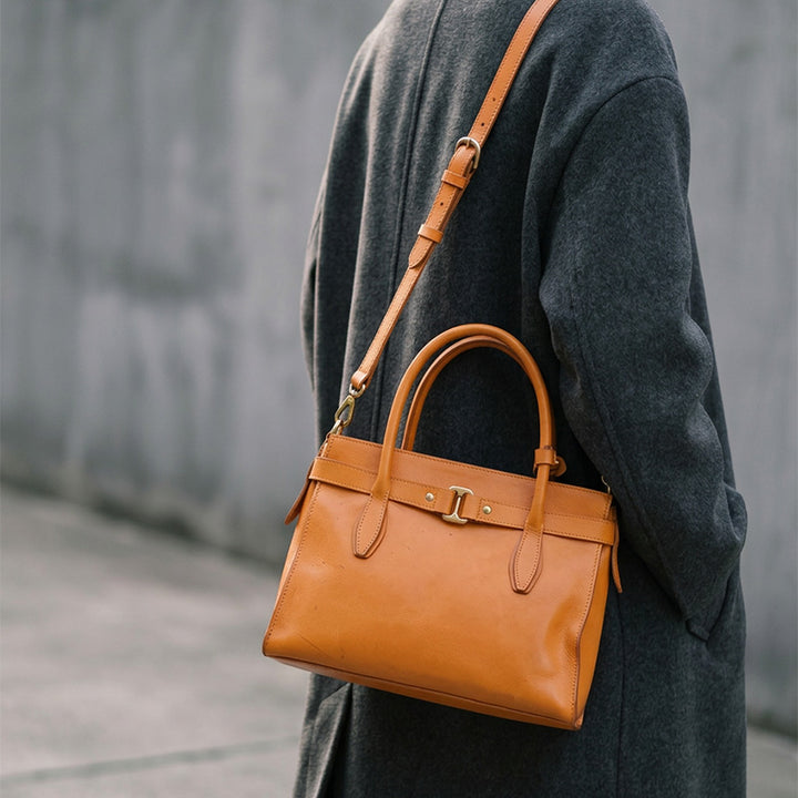 Woman carrying a structured leather top handle bag in tan yellow as a crossbody on the street