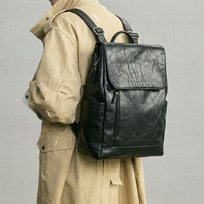 Minimalist vegetable tanned leather backpack in black with magnetic flap closure and luggage sleeve
