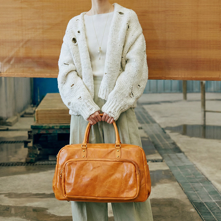 A large vegetable-tanned leather duffle bag in sunset yellow, featuring gold hardware and dual top handles.