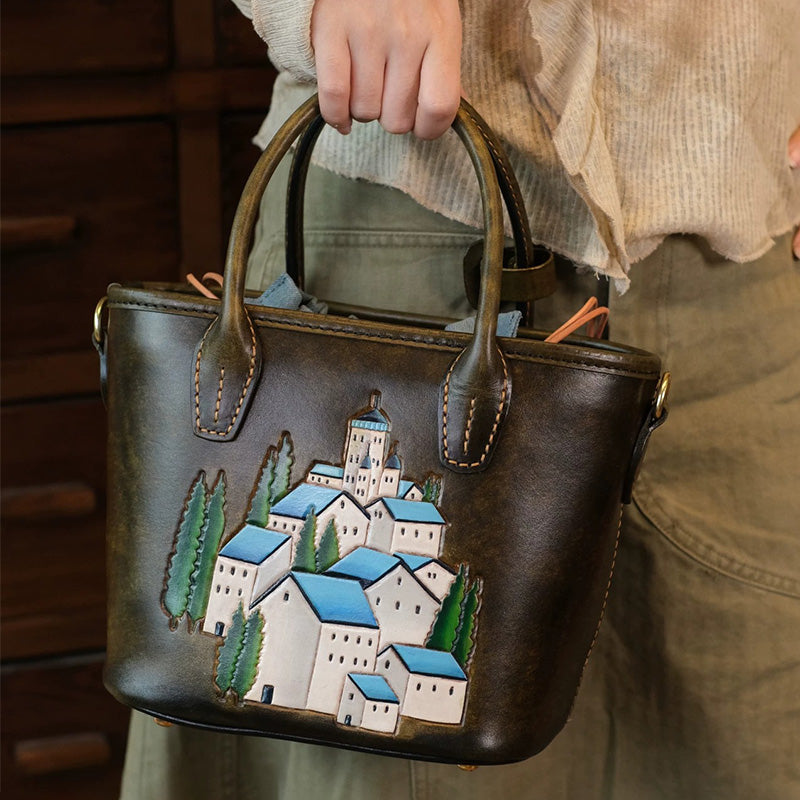 Woman holding an olive-brown leather tote with hand-tooled village artwork.