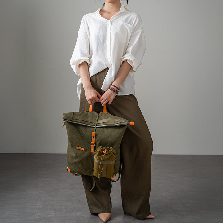 Olive waxed canvas roll-top backpack with leather trim, carried by hand