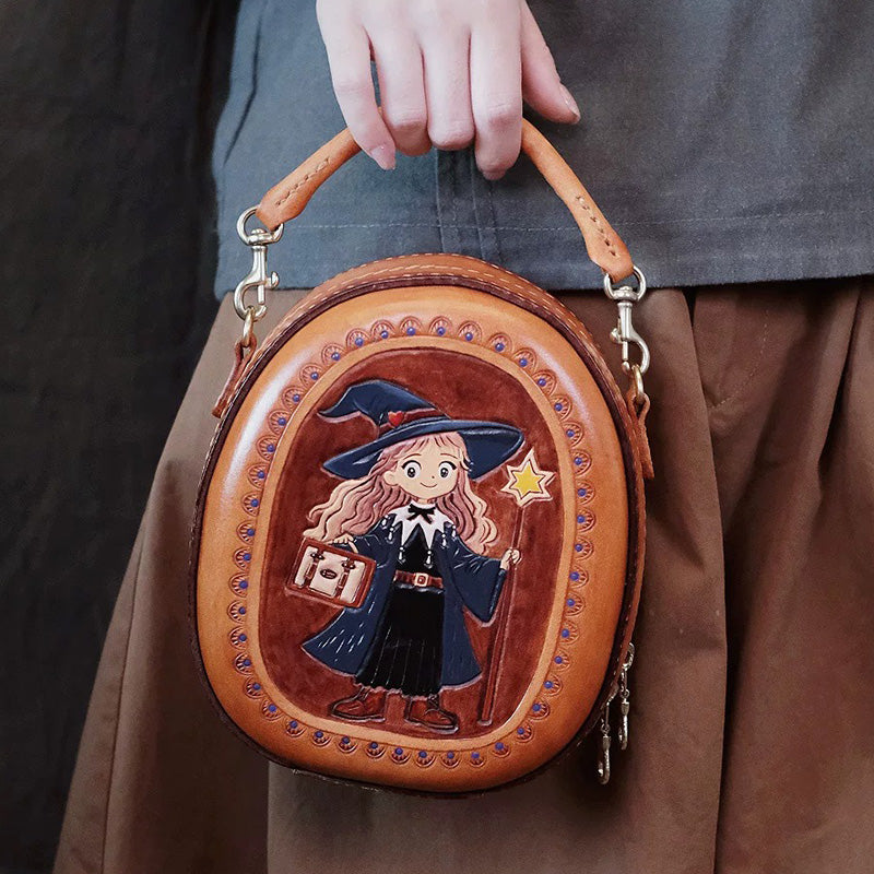 A model holds a brown oval leather crossbody bag with witch artwork by its top handle.