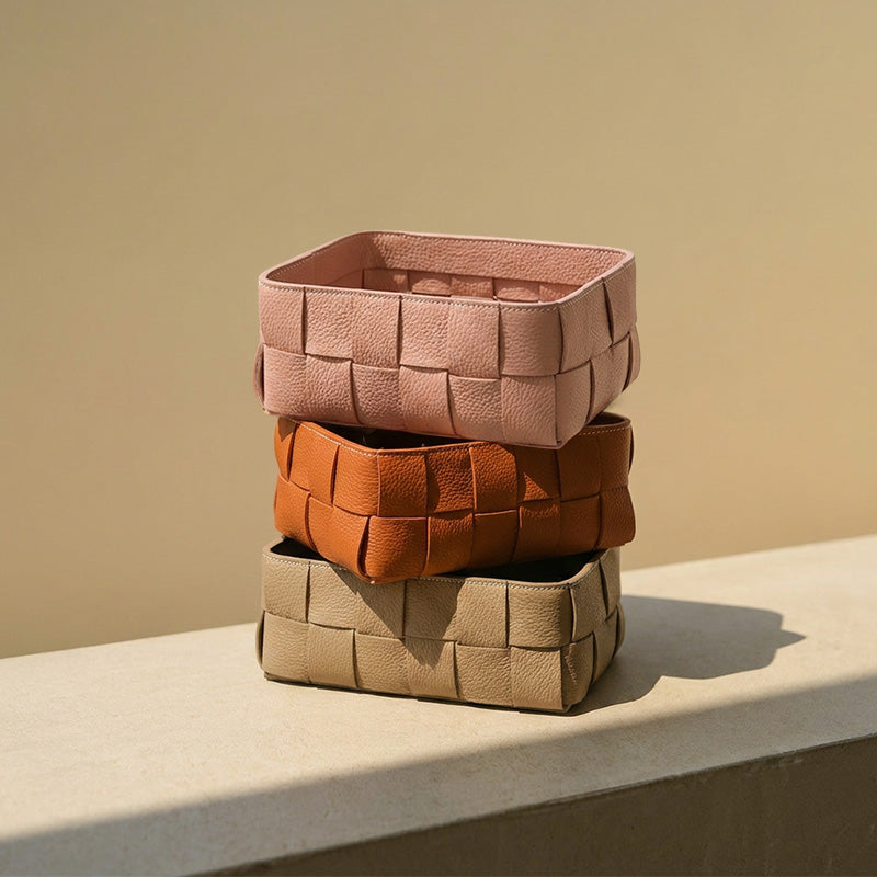 Three woven leather storage baskets stacked in pink, orange, and brown tones